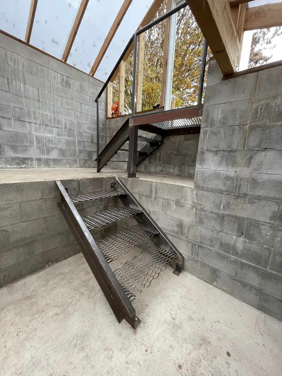 Steel stairs with expanded metal treads going down into a greenhouse
