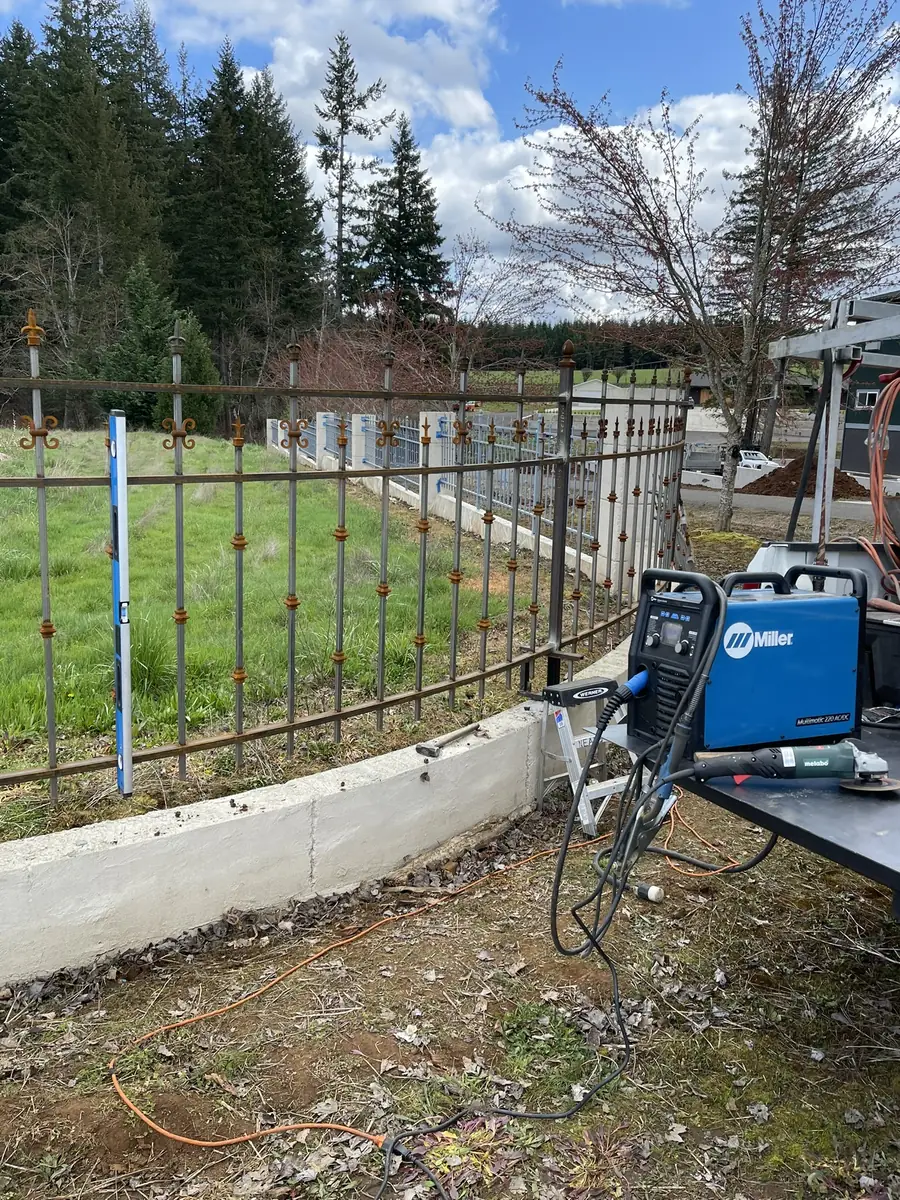 Iron fence on a concrete wall with a welder set up beside it