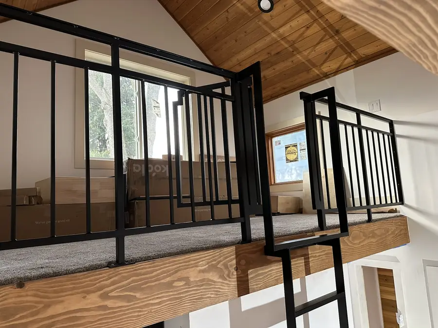Black steel loft railing and ladder under a wood ceiling