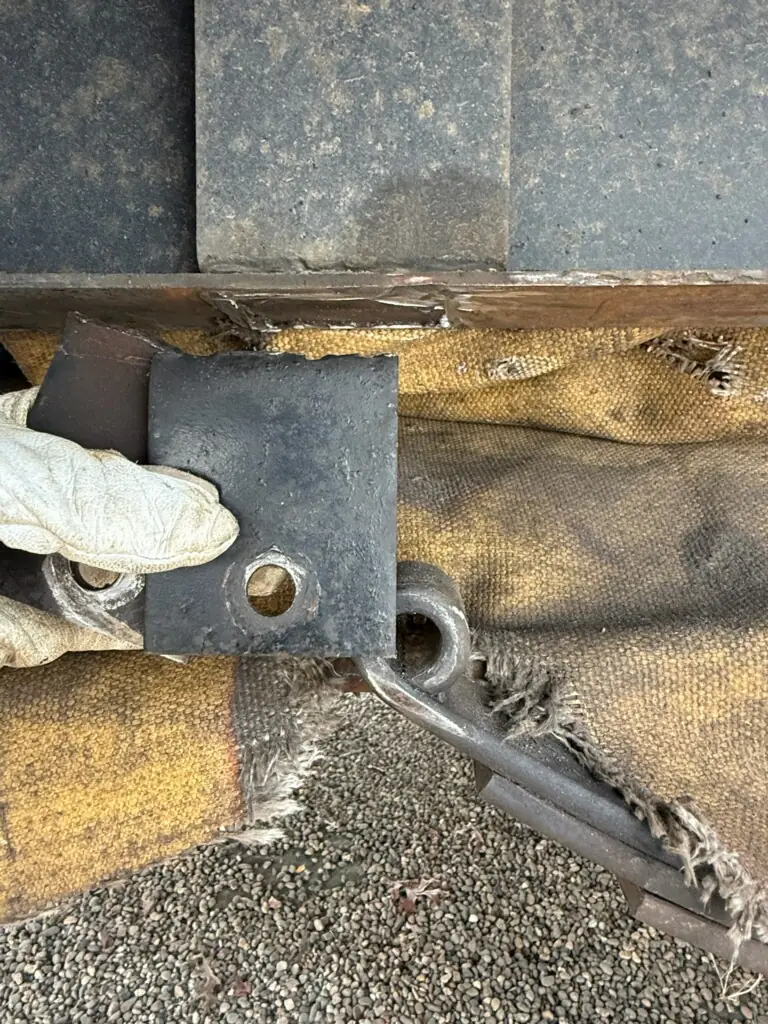 Worn-out RV spring hanger held up beside the leaf spring, with a welding blanket behind it