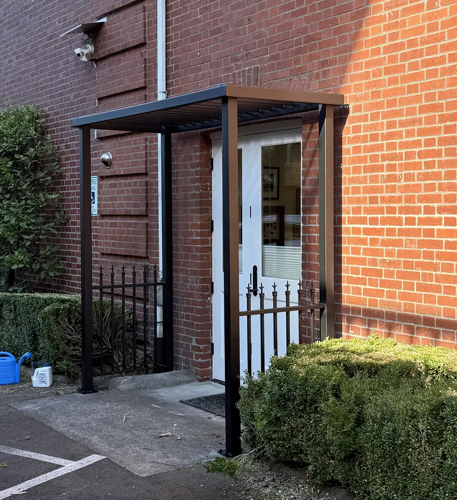 Black steel entry canopy with railing sections at a brick building
