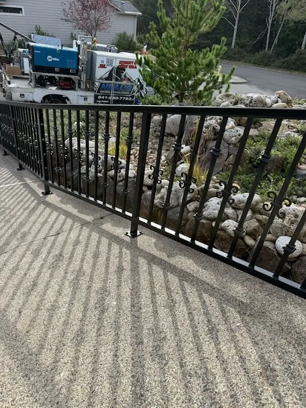 Long run of black steel railing with scroll pickets along a steep driveway, Neal's welding truck parked behind it